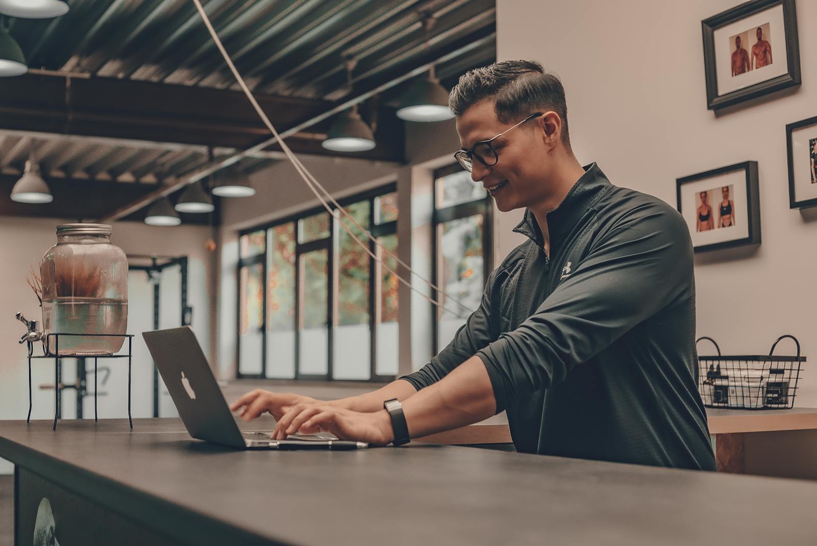 Smiling man in sportswear using a laptop indoors, conveying a modern workspace atmosphere.